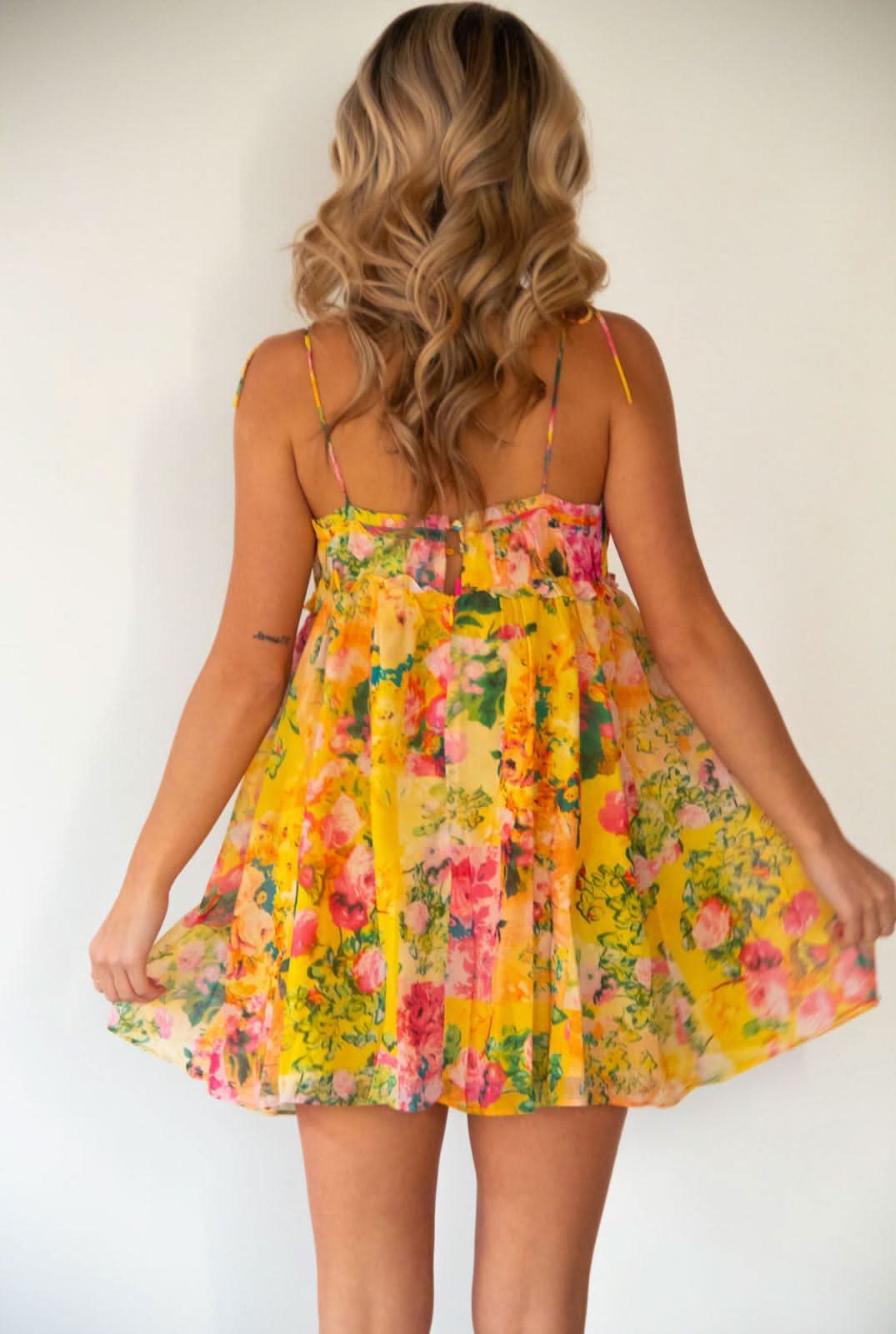Back view showing tie straps and full skirt of yellow floral mini dress