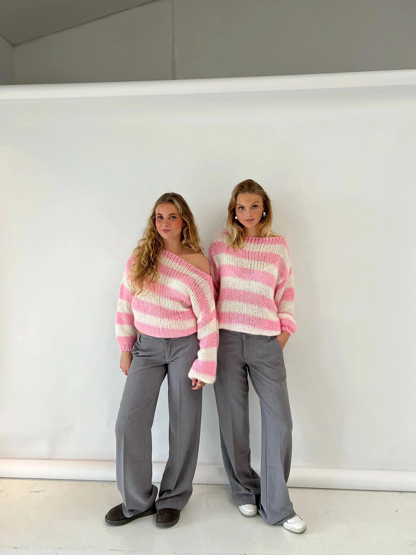 Pink and cream striped knit sweater on two models with gray trousers