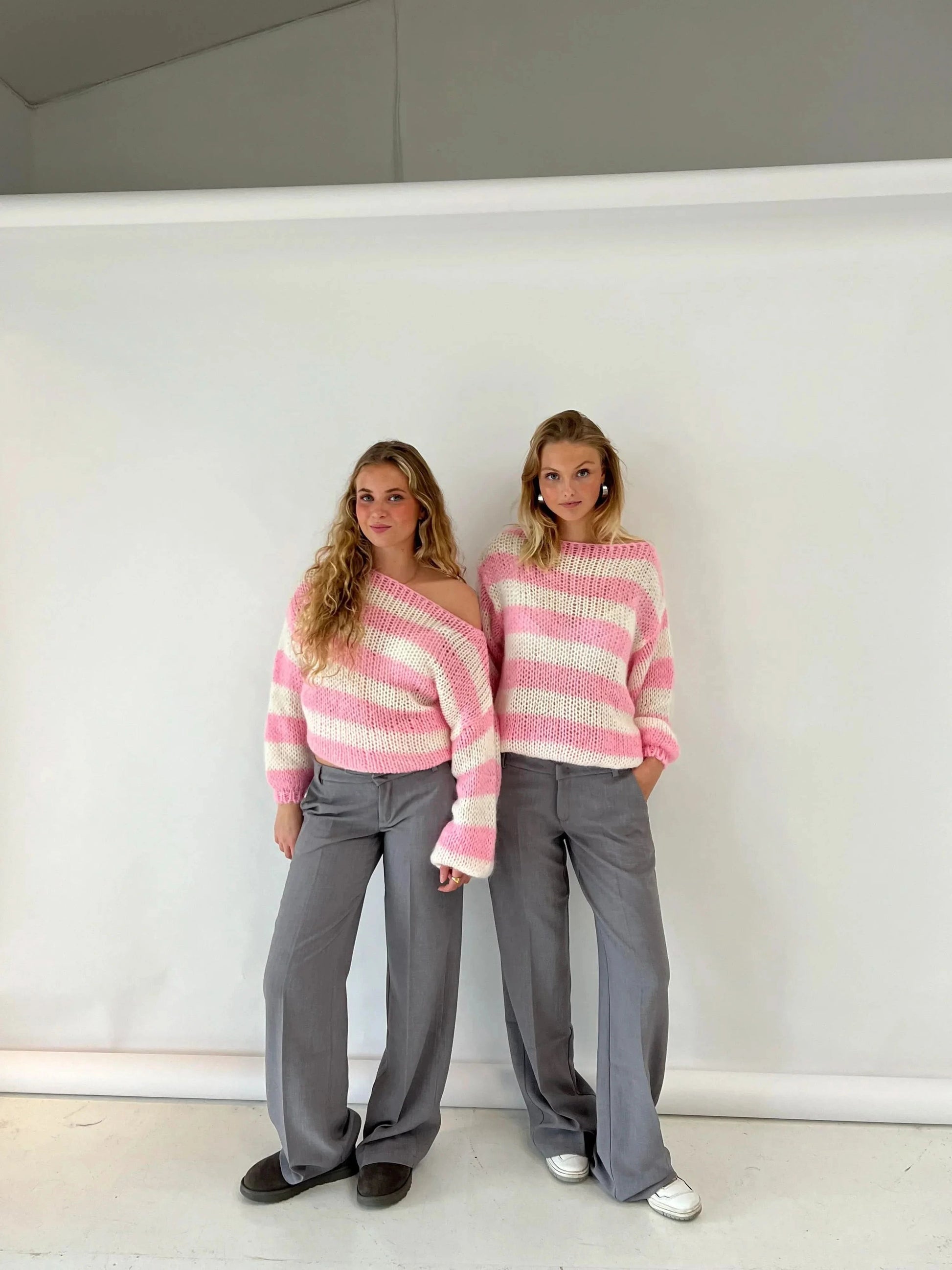 Pink and cream striped knit sweater on two models with gray trousers