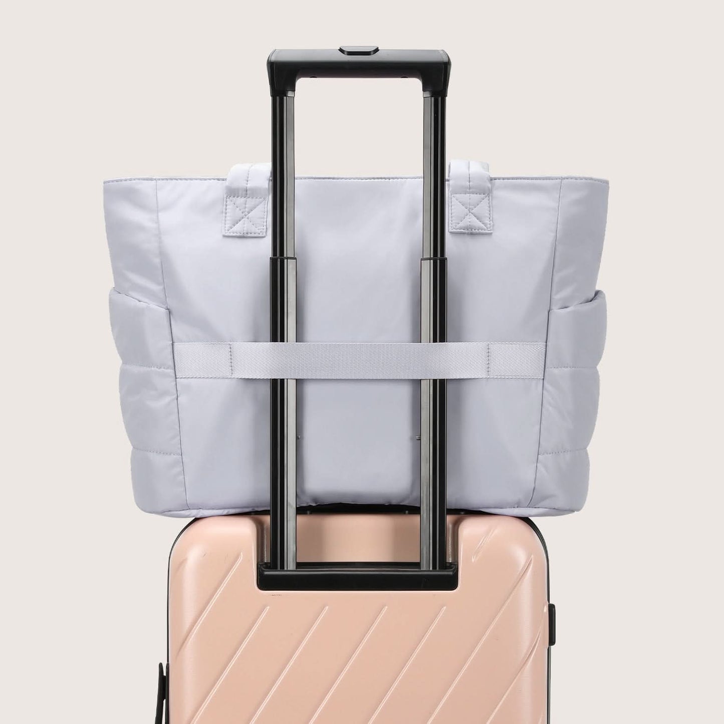 Light gray quilted tote on luggage handle showing travel-ready attachment strap