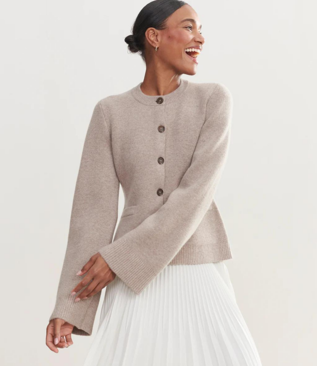 Beige crew neck cardigan with brown buttons and ribbed cuffs, paired with white pleated skirt