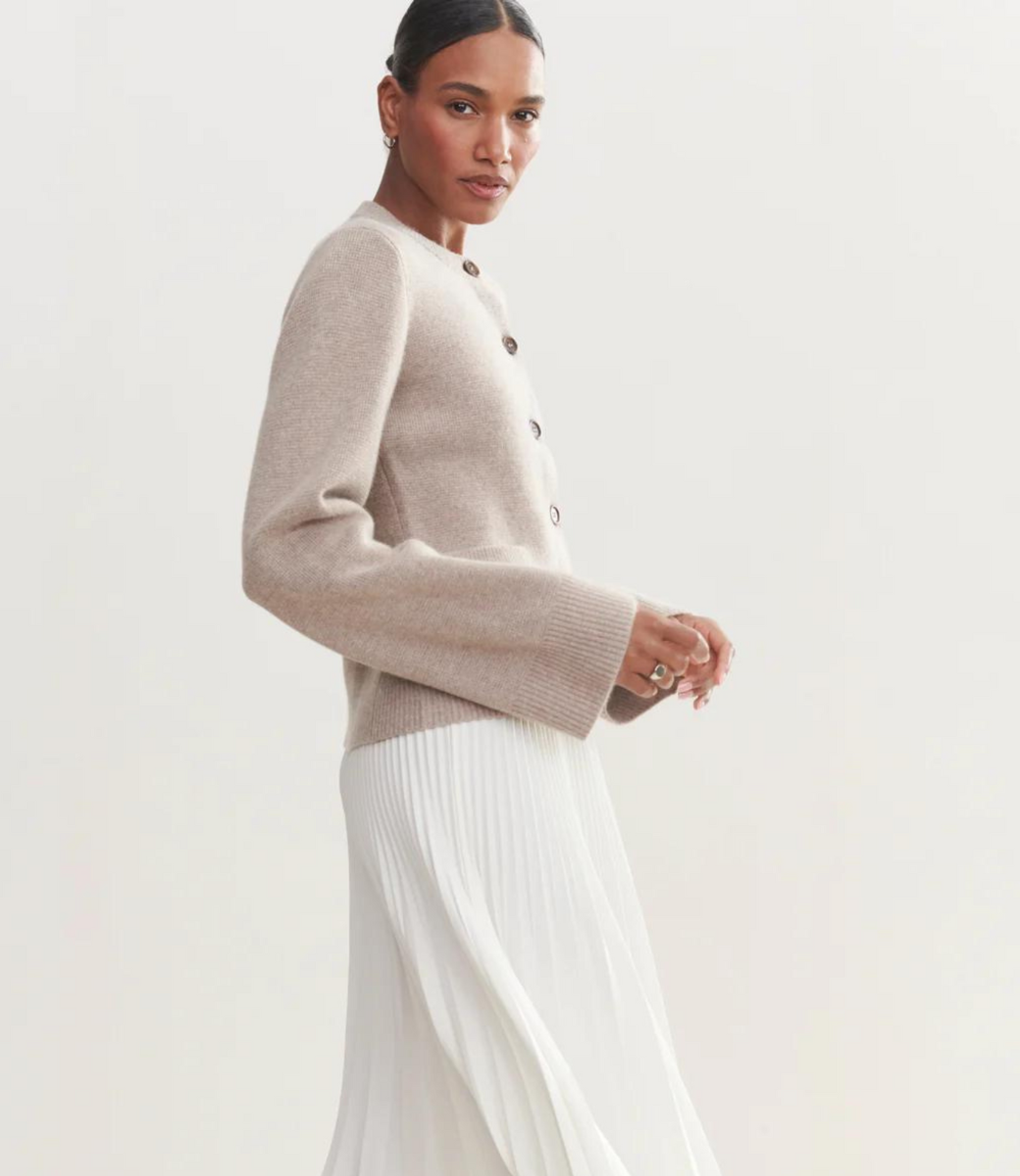 Beige crew neck cardigan with brown buttons and ribbed cuffs, paired with white pleated skirt