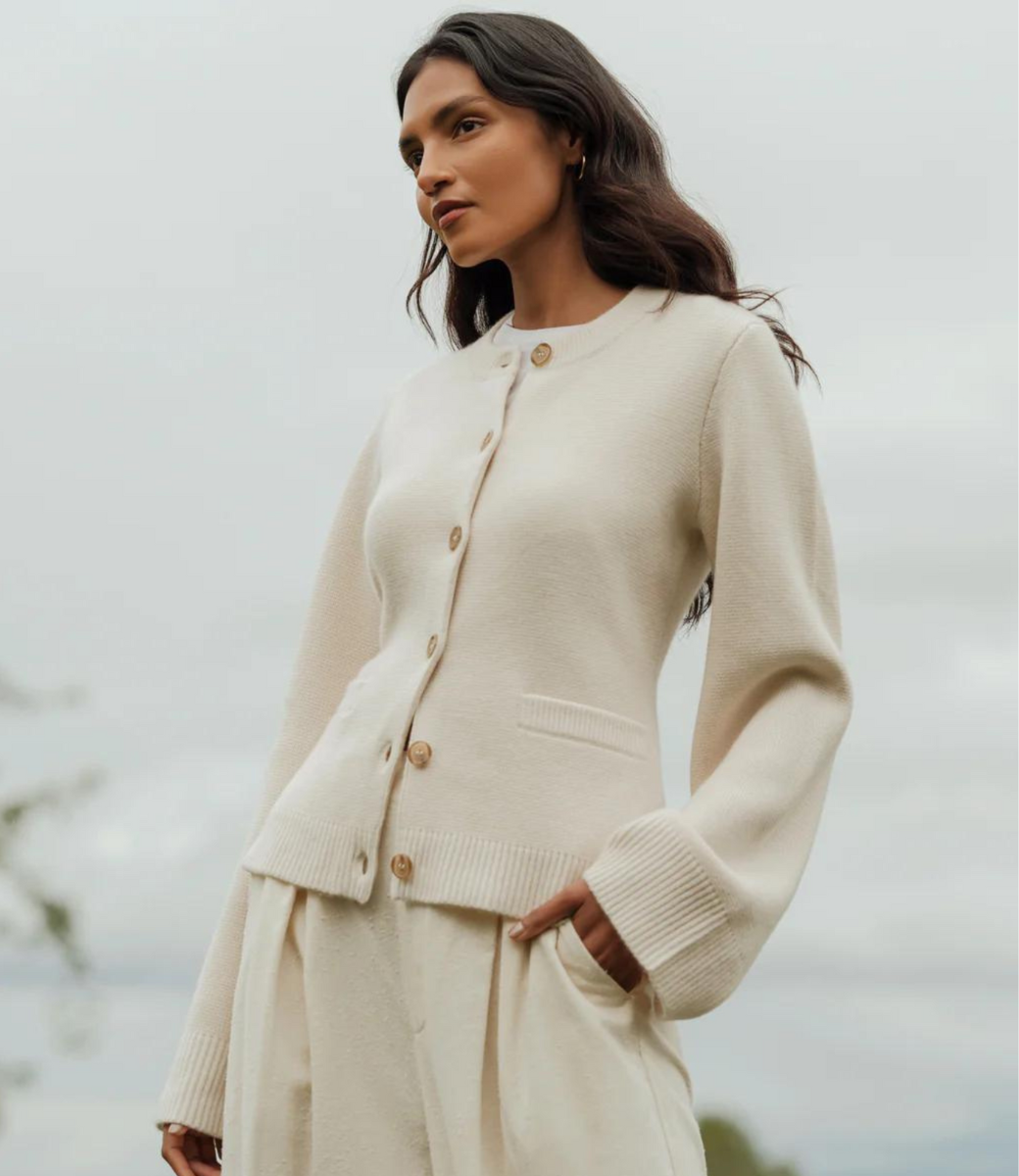 Cream button-front cardigan with ribbed cuffs and waist detail, worn with matching pleated skirt