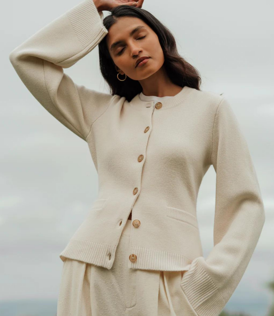 Cream button-front cardigan with ribbed cuffs and waist detail, worn with matching pleated skirt