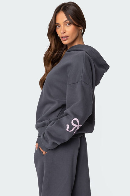 Back view of charcoal gray drop-shoulder hoodie with pink bow graphic detail