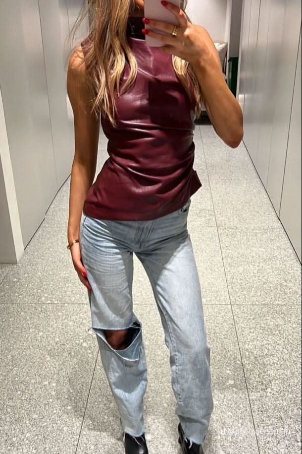 Burgundy sleeveless tank with high neck and ruching worn with ripped light-wash jeans