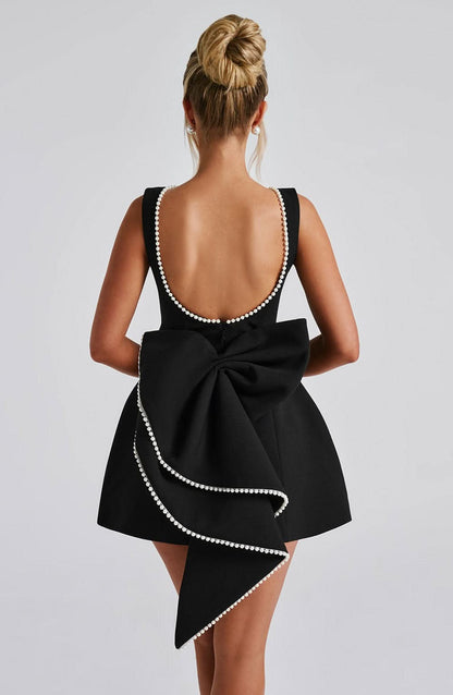 Black mini dress with pearl-trimmed open back and oversized bow detail