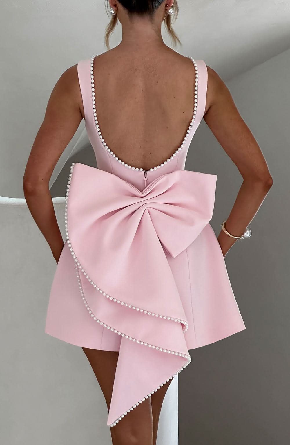 Blush pink mini dress back view with pearl trim and asymmetrical bow