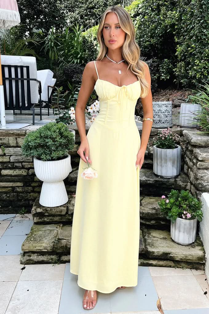 Pale yellow spaghetti strap maxi dress with ruched bodice in outdoor garden setting