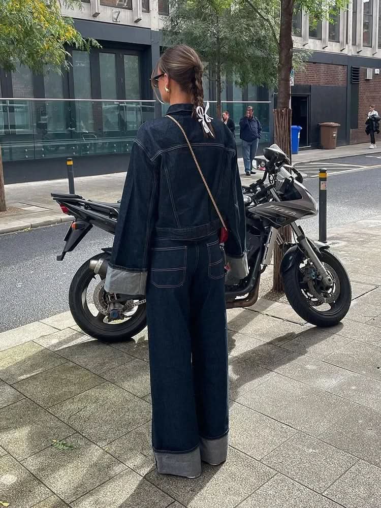 Back view of dark denim jacket with gray cuffed sleeves and wide-leg dark denim pants