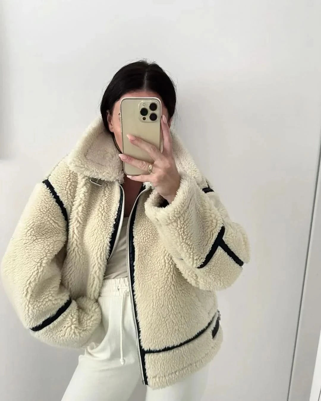 Front close-up of cream teddy coat showing black contrast trim and zip fastening