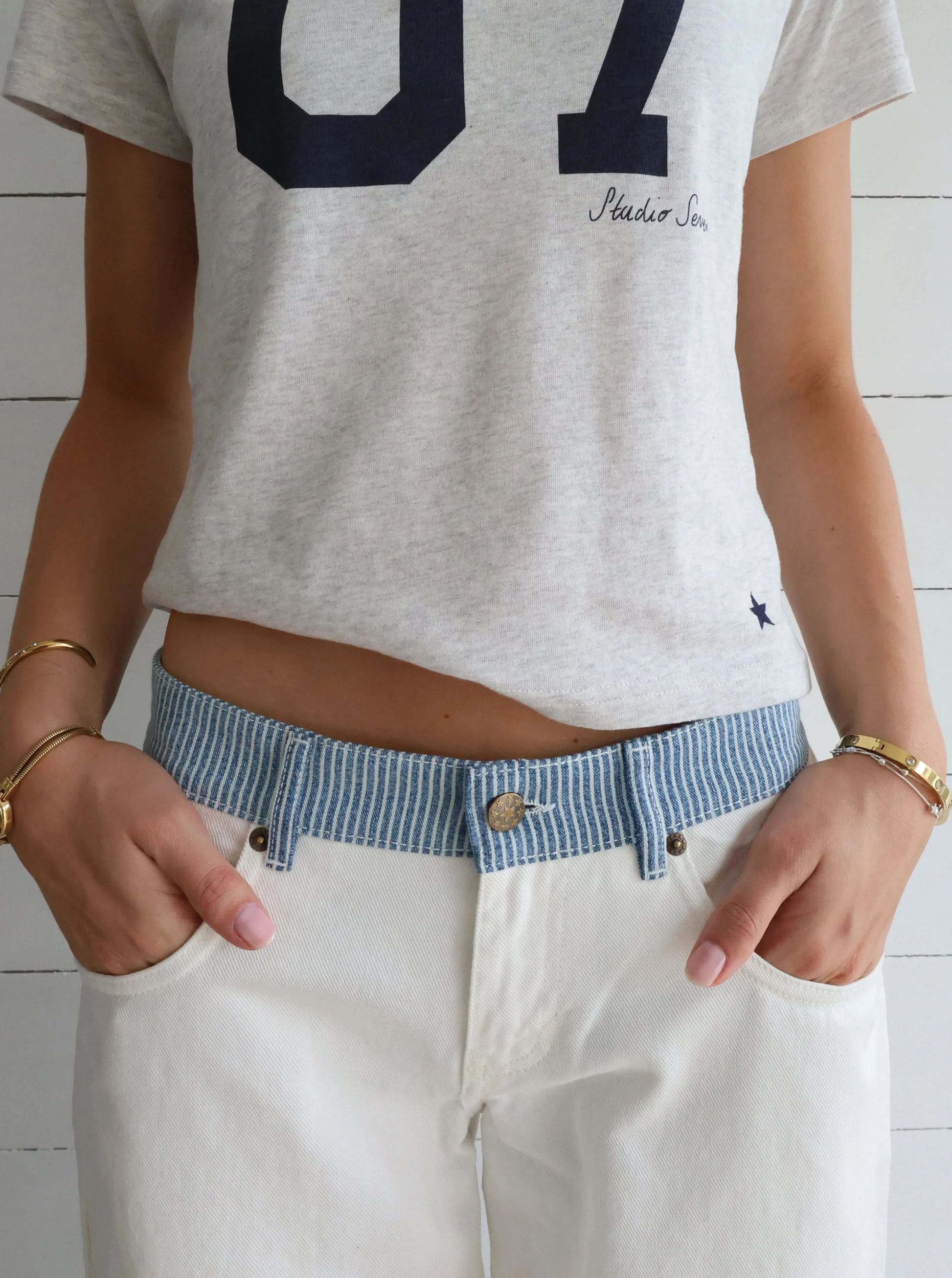 Close-up of white jeans waistband with blue striped trim and metal button detail