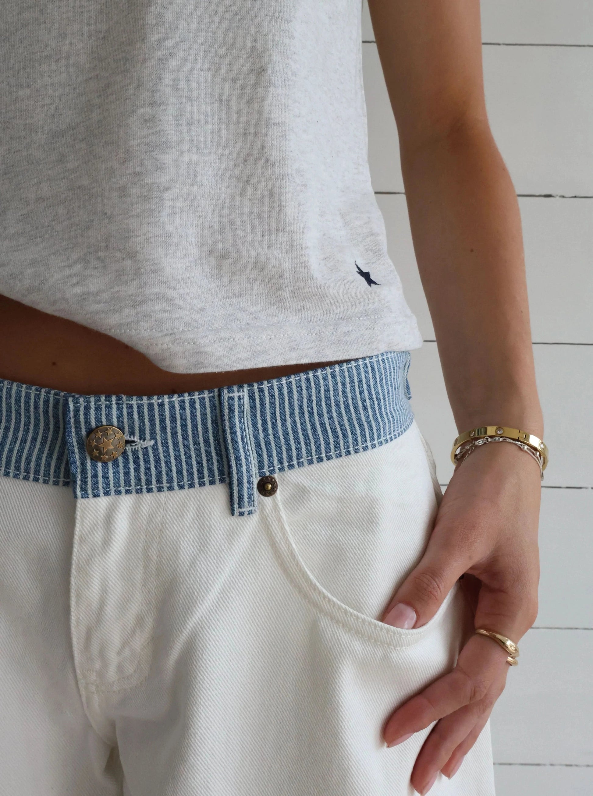 White denim jeans pocket detail with blue striped waistband and brass hardware