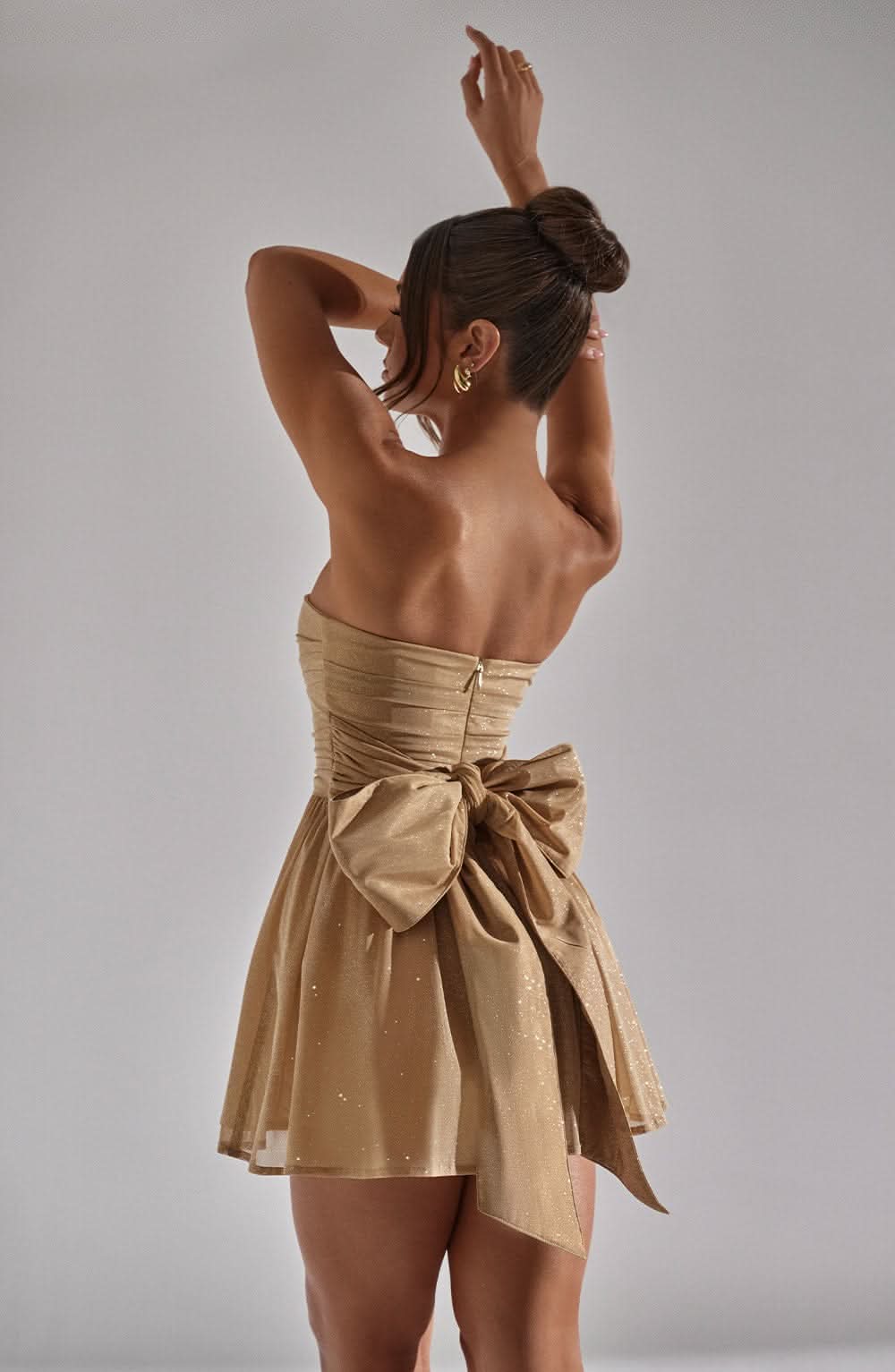 Back angle of champagne sparkle strapless mini dress with oversized bow