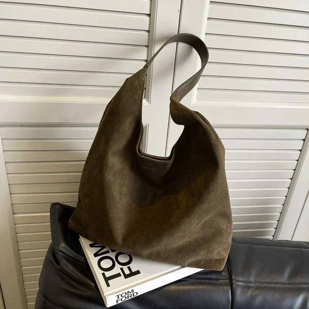 Olive green suede tote bag with brown handles on magazine stack