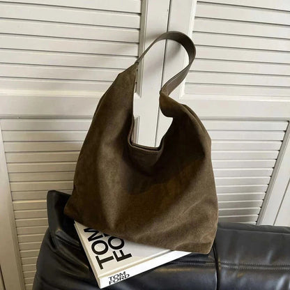 Olive green suede tote bag with brown handles on magazine stack