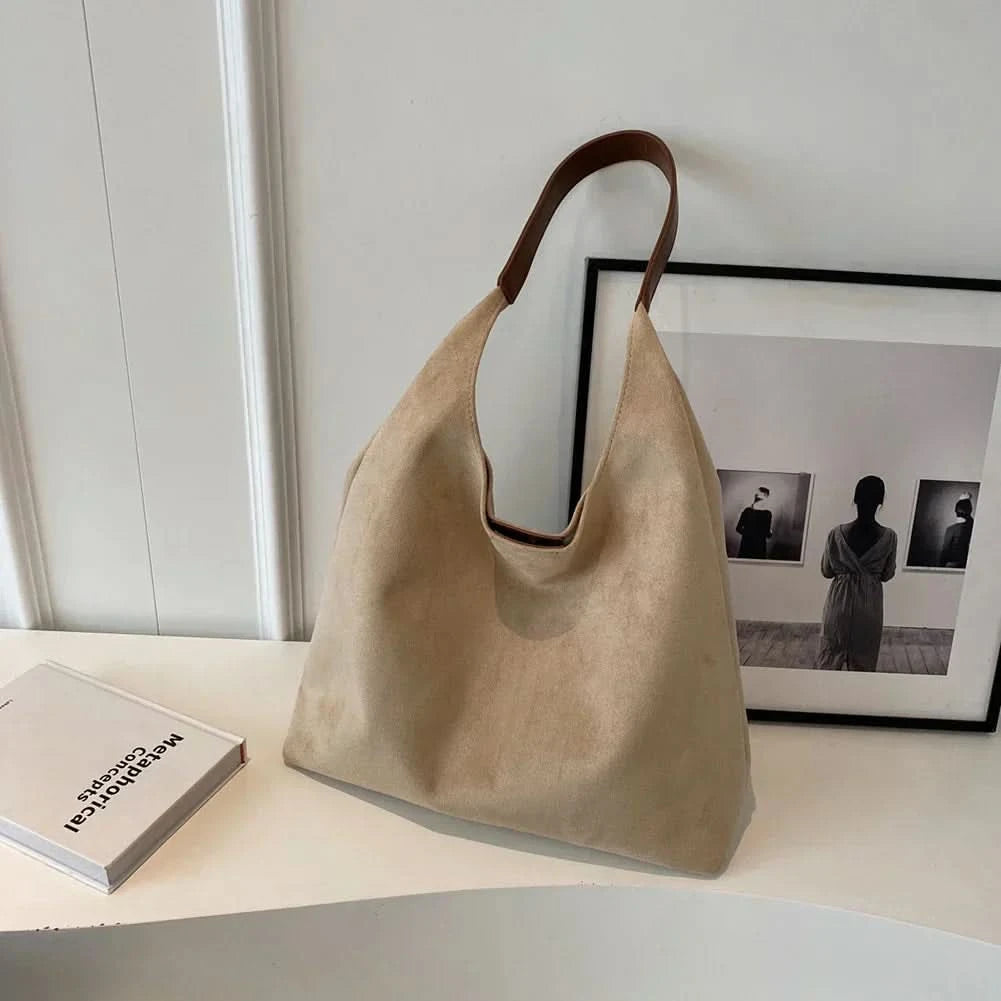 Beige suede tote bag with brown handles displayed on table