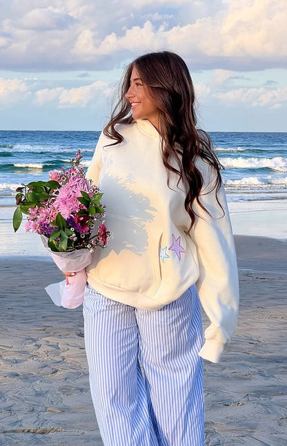 Back view of cream hoodie showing blue and pink decorative stars on fleece fabric at ocean