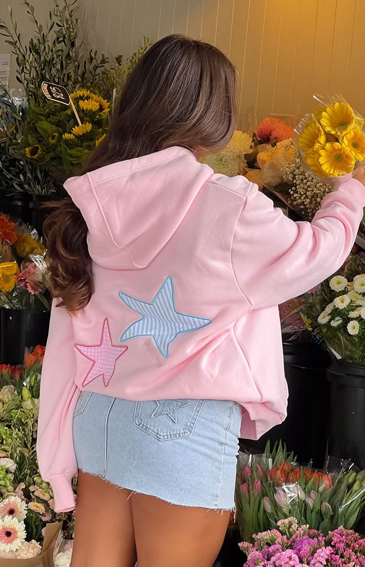Pink oversized fleece hoodie with star appliqués worn indoors showing pocket and fit detail