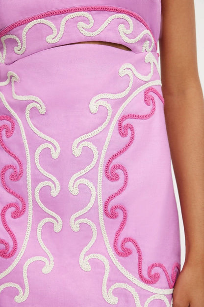 Close-up of intricate white and hot pink beaded embroidered scrollwork on pink dress fabric
