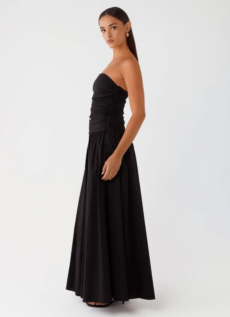 Black strapless maxi dress with ruched torso and flowing skirt, side profile view