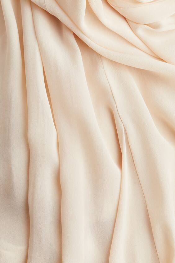 Close-up of soft pleated cream chiffon fabric on flowing maxi dress skirt
