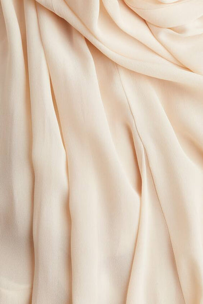 Close-up of soft pleated cream chiffon fabric on flowing maxi dress skirt