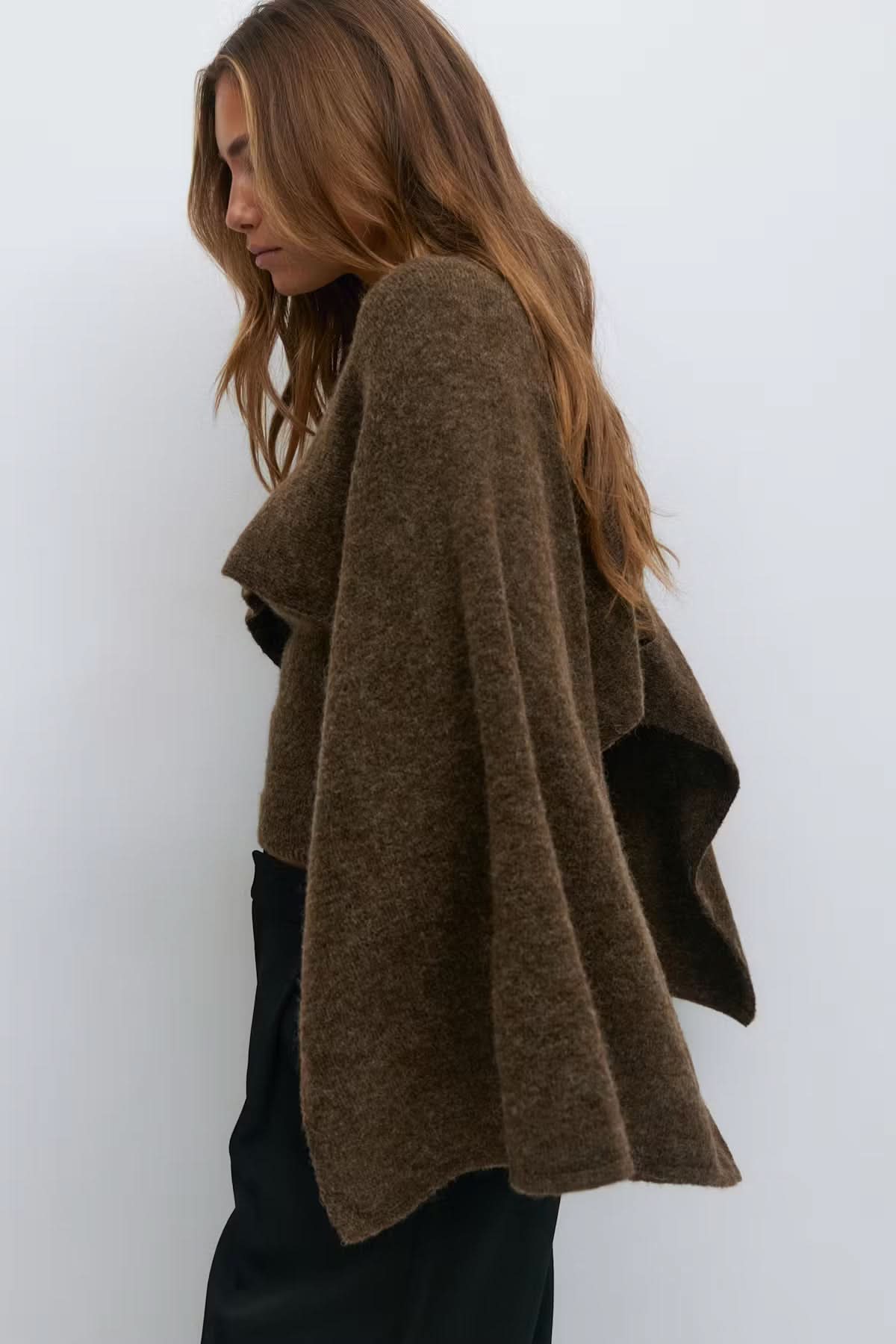 Side view of olive knitted cape with flowing asymmetrical hem detail